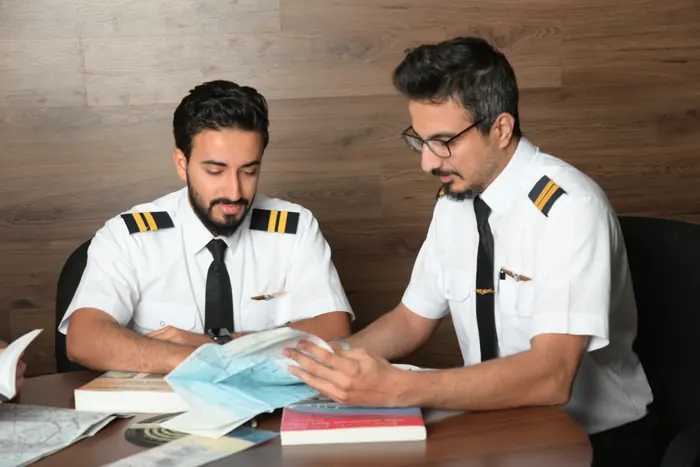 Two trainees reviewing navigation charts at a study table