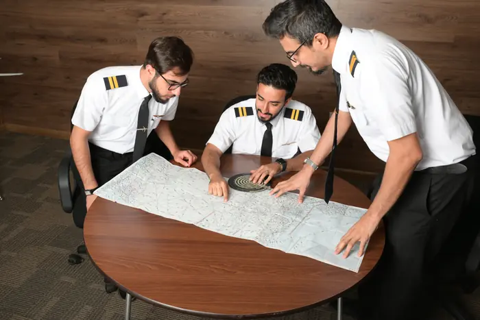 An instructor briefing trainees over a navigation chart