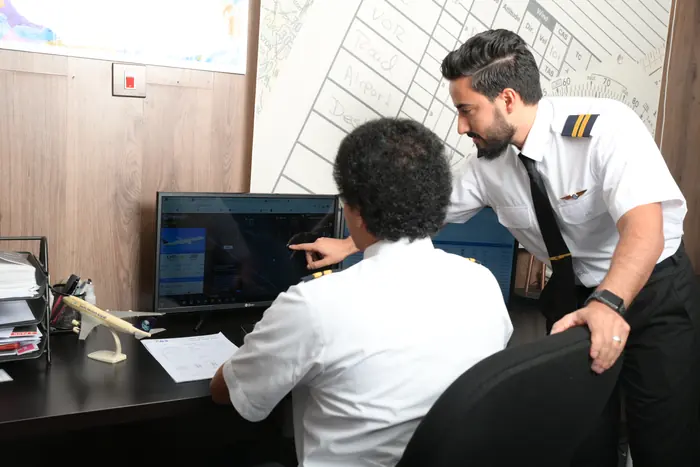 An instructor guiding a trainee at a flight planning workstation
